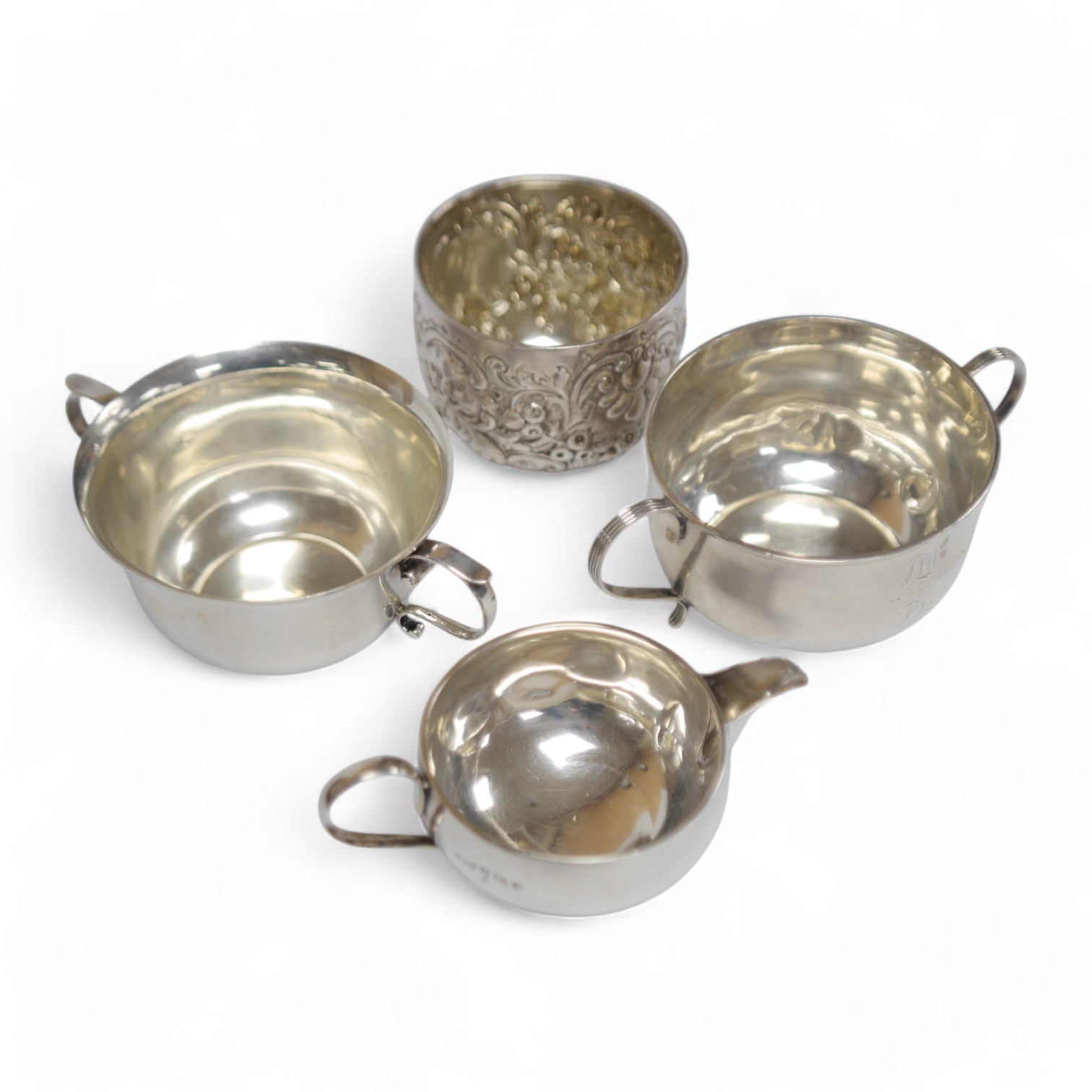 A late Victorian silver porringer, London, 1897, height 61mm, an Edwardian silver porringer, a late Victorian repousse silver sugar bowl and a George V silver cream jug by Hukin & Heath, 17.1oz. Condition - poor to fair